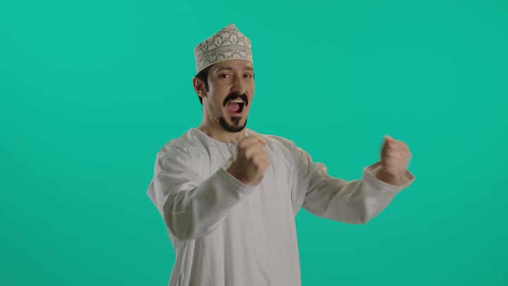 تعابير الفرحة بالانتصار , رجل عربي خليجي عماني يرتدي دشداشة بيضاء و كمة مطرزة يقفل قبضة اليد و يحرك ذراعة للامام و الخلف في الهواء اشارة للحماس  , ايماءات التهليل و التشجيع