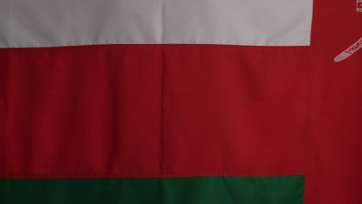 الوقوف أمام الكاميرا، نظرة الفخر والعزة، شاب عربي خليجي عماني يرتدي الداشداشة البيضاء والكمة المطرزة يرفع العلم العماني على الأكتاف، تعابير السعادة والسرور واضحة على الوجه.