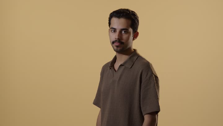 Standing firmly and confidently, an Arab Gulf Saudi man dressed in casual attire crosses his arms and looks at the camera, with expressions of happiness and confidence.