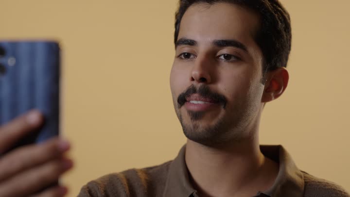 اجراء مكالمات الفيديو باستخدام العديد من التطبيقات المختلفة , رجل عربي خليجي سعودي يرتدي الزي الكاجوال يحمل الهاتف المحمول في التواصل المباشر مع الاهل و الاصدقاء , تعابير السعادة و الفرحة