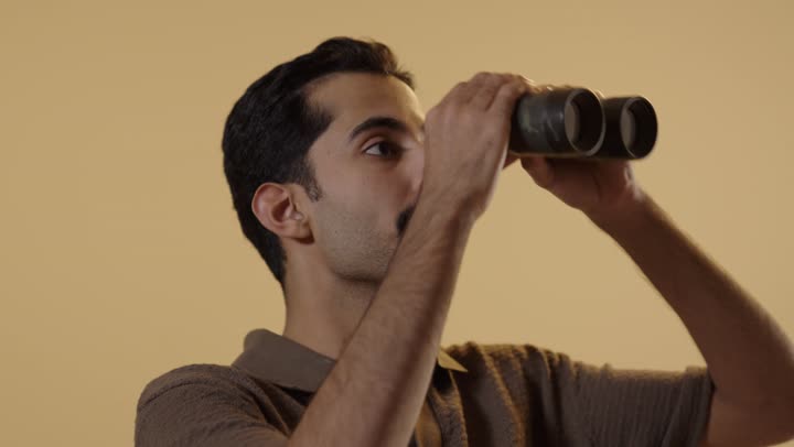 النظر الى شئ ما بعيد جداً , رجل عرب خليجي سعودي يرتدي الزي الكاجوال يحمل المنظار المقرب لرؤية اوضح, تعابير الاعجاب الشديد و الانبهار