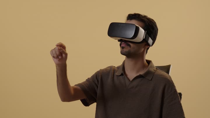 Moving fingers in the air is a sign of focus and immersion in the virtual world. An Arab Gulf Saudi man dressed in casual attire wears glasses to simulate the real world, with expressions of astonishment and amazement.