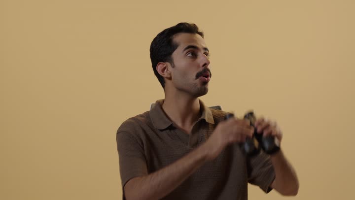 رجل عربي خليجي سعودي يرتدي الزي الكاجوال يحمل المنظار المقرب للاشياء البعيدة , تعابير الدهشة و الذهول , النظر الى شئ في السماء البعيدة