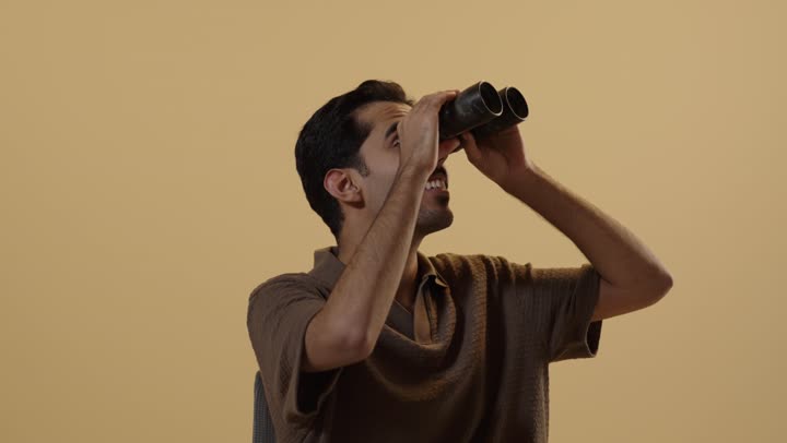 Looking at something far away using a telescope to see distant objects clearly, an Arab Gulf Saudi man wearing casual attire holding lenses to magnify the image, gestures of amazement and happiness.