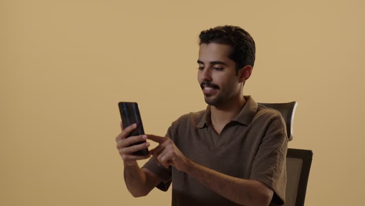 Browsing on a mobile phone and spending special times on various applications, an Arab Gulf Saudi man wearing casual attire holding a mobile phone, expressions of joy and happiness.