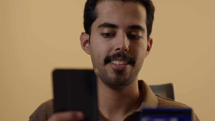 ايماءات السعادة و الحماس اثناء تسجيل الارقام السرية الخاصة بالبطاقة البنكية , رجل عربي سعودي خليجي يرتدي الزي الكاجوال يحمل الهاتف المحمول , تطبيقات التسوق الالكتروني عبر الانترنت