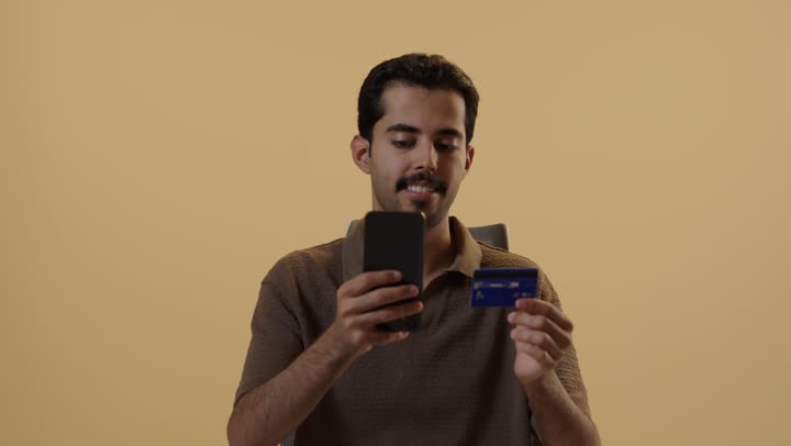 التطور المذهل في التطبيقات الخاصة بالتسوق الالكتروني , رجل عربي خليجي سعودي يرتدي الزي الكاجوال يقوم بادخال الارقام السرية الخاصة بالبطاقة البنكية , ايماءات السعادة و الابتسام