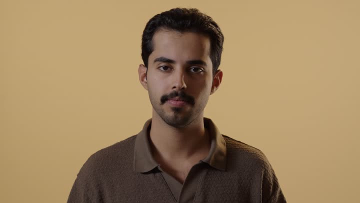 A young Arab Gulf Saudi man wearing casual attire raises his arm with an open hand in front of the camera as a sign to stop, with expressions of anger and annoyance, do not come closer.