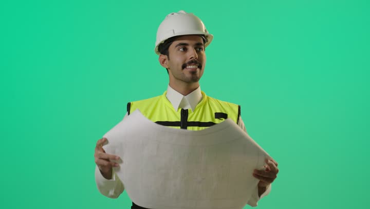 Monitoring work at construction sites, a Saudi Gulf Arab engineer wearing a helmet and reflective vest holding the construction plan, gestures of happiness and satisfaction with the progress of the work.