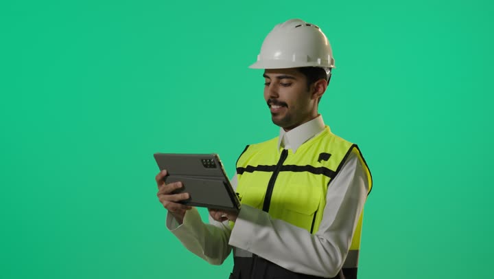 تعابير السعادة و السرور في مواقع العمل , مهندس عربي خليجي سعودي يرتدي الزي الخاص بالمهندسين للحفاظ على السلامة , استخدام الجهاز اللوحي في انجاز المهمات بسهولة