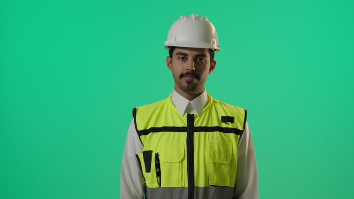 مهندس عربي خليجي سعودي يرتدي خوذة الامان و الصديري العااكس للضوء في اثناء العمل , رفع اصبع الابهام لاعلى مع ضم باقى الاصابع علامة على الاعجاب بشئ ما , تعابير السرور و الفرحة