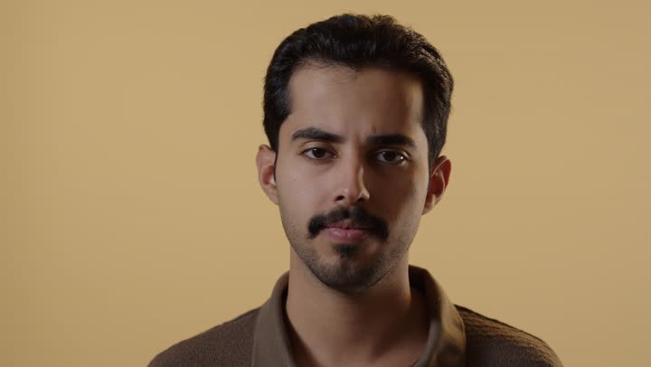 رجل عربي خليجي سعودي يرتدي الزي الكاجوال يشعر بالضيق و الانزعاج, وضع اصبع السبابة امام الفم في اشارة الي السكوت و الامتناع عن الكلام , تعابير التجهم و العبوس