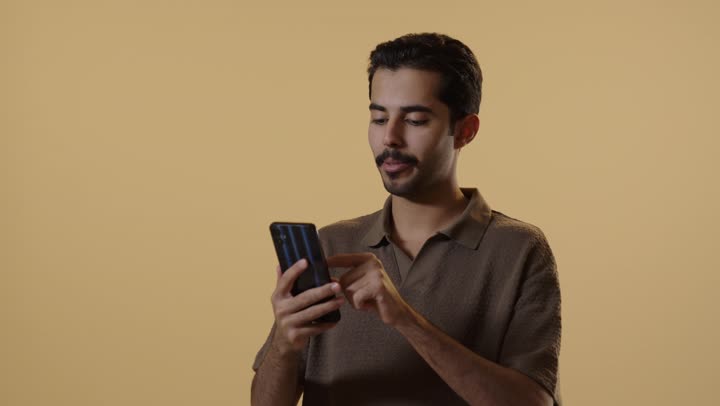 اجراء المكالمات الهاتفية الجماعية الخاصة بالعمل من اي مكان بسهولة , شاب عربي خليجي سعودي يرتدي الزي الكاجوال يستخدم التطبيقات الخاصة بالمحادثات الصوتية و الفيديو , تعابير السعادة و البهجة