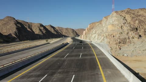 Construction of a new road, desert of the Kingdom of Saudi Arabia, drone footage of an asphalt road between towering rocky mountains, traffic of cars outside the city.