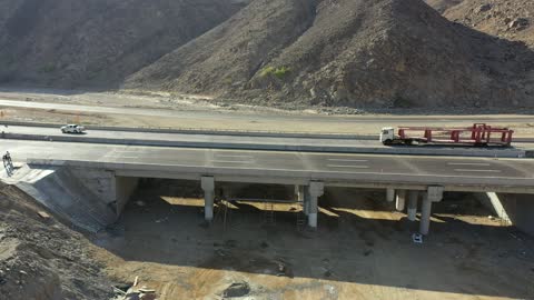 Traffic of cars outside the city, construction of a new road, desert of the Kingdom of Saudi Arabia, drone footage of an asphalt road between towering rocky mountains.