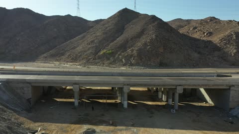 Traffic of cars outside the city, construction of a new road, desert of the Kingdom of Saudi Arabia, drone footage of an asphalt road between towering rocky mountains.