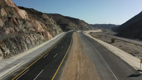 حركة مرور السيارات خارج المدينة، إنشاء طريق جديد، صحراء المملكة العربية السعودية، تصوير درون لطريق اسفلتي بين الجبال الحجرية الشاهقة