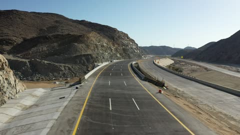 حركة مرور السيارات خارج المدينة، إنشاء طريق جديد، صحراء المملكة العربية السعودية، تصوير درون لطريق اسفلتي بين الجبال الحجرية الشاهقة