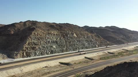 Construction of a new road, desert of the Kingdom of Saudi Arabia, drone footage of an asphalt road between towering rocky mountains, traffic of cars outside the city.