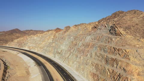Traffic of cars outside the city, construction of a new road, desert of the Kingdom of Saudi Arabia, drone footage of an asphalt road between towering rocky mountains.