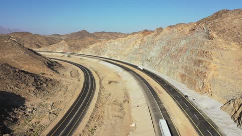 إنشاء طريق جديد، صحراء المملكة العربية السعودية، تصوير درون لطريق اسفلتي بين الجبال الحجرية الشاهقة، حركة مرور السيارات خارج المدينة