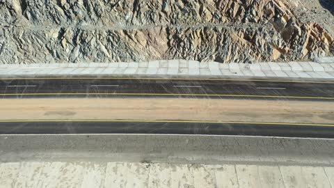 Desert of the Kingdom of Saudi Arabia, drone footage of an asphalt road between towering rocky mountains, traffic of cars outside the city.