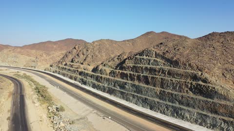 Construction of a new road, desert of the Kingdom of Saudi Arabia, drone footage of an asphalt road between towering rocky mountains, traffic of cars outside the city.