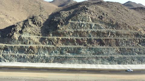 Desert of the Kingdom of Saudi Arabia, drone footage of an asphalt road between towering rocky mountains, traffic of cars outside the city.