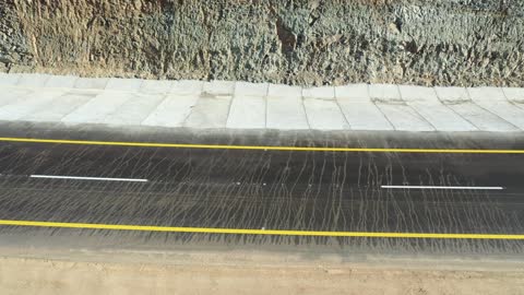Construction of a new road, desert of the Kingdom of Saudi Arabia, drone footage of an asphalt road between towering rocky mountains, traffic of cars outside the city.