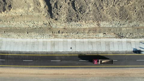 Desert of the Kingdom of Saudi Arabia, drone footage of an asphalt road between towering rocky mountains, traffic of cars outside the city.