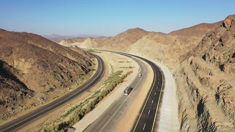 Desert of the Kingdom of Saudi Arabia, drone footage of an asphalt road between towering rocky mountains, traffic of cars outside the city.