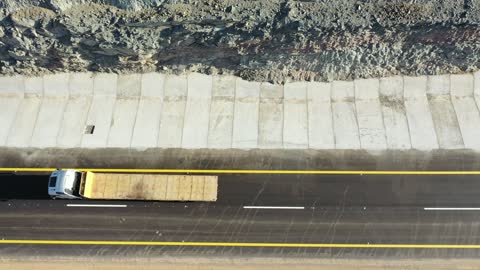 Traffic of cars outside the city, construction of a new road, desert of the Kingdom of Saudi Arabia, drone footage of an asphalt road between towering rocky mountains.
