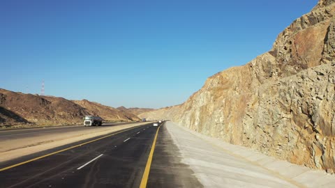 Desert of the Kingdom of Saudi Arabia, drone footage of an asphalt road between towering rocky mountains, traffic of cars outside the city.