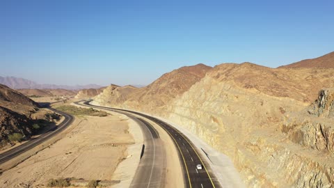 Construction of a new road, desert of the Kingdom of Saudi Arabia, drone footage of an asphalt road between towering rocky mountains, traffic of cars outside the city.