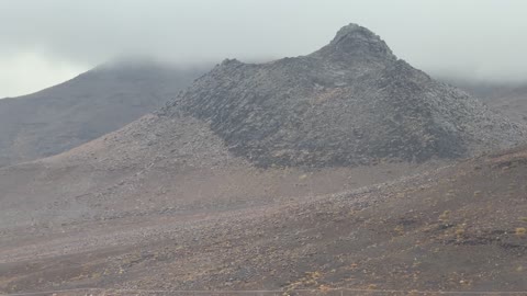 تساقط البرد (حبات الثلج الصغيرة) فوق منطقة الحرات البركانية في تبوك، الجو الشتوي الضبابي فوق الجبل في سماء مدينة حرة تبوك في المملكة العربية السعودية