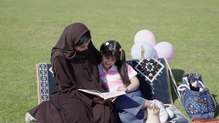 امرأة عربية خليجية سعودية محجبة ترتدي عباءة سوداء تجلس بجوار ابنتها و تحكي لها القصص التاريخية الممتعة و المسلية عن الاجداد , والد عربي خليجي سعودي يلعب كرة القدم مع ابنه , الشعور بالمحبة و الألفة بين افراد العائلة