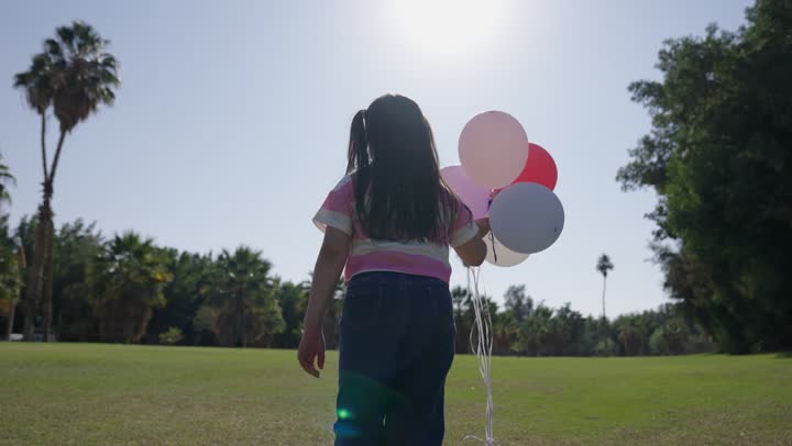 تعدد انواع السياحة الداخلية في المملكة , طفلة عربية خليجية سعودية ترتدي الزي الكاجوال ترفع مجموعة ملونة من البالونات في خفة و مرح , الاستمتاع بالاجواء الدافئة و السماء الصافية