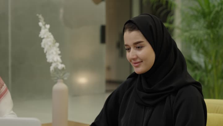 لتعاون والتفاعل الجماعي من أجل تحقيق أهداف الشركة ومعالجة المشكلات، مفهوم الإدارة المتعاونة، رجل عربي خليجي سعودي يرتدي الثوب و الشماغ يجلس امام الحاسب المحمول مع زميلتة يتناقش في أمور العمل، إنجاز المهام المكتبية اليومية