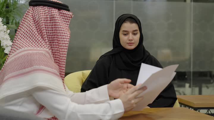 شرح المهام المطلوبة، تنظيم وادارة جدول مفهوم العمل, التعاون والتفاهم بين الفريق, تبادل الخبرات والاتفاقيات الناجحة, رجل عربي خليجي سعودي يرتدي الثوب الابيض يجلس برفقة زميلته يقوم بشرح العمل