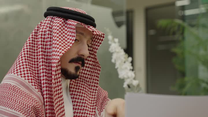 اعداد التقارير الخاصة بالعمل،تصوير مقرب لرجل عربي خليجي سعودي يرتدي الثوب و الشماغ يحمل بيده مجموعة من الاوراق البيضاء، مراجعة ومتابعة الخطط والمشاريع المكتبية بإيماءات التركيز، التدقيق في قراءة الملاحظات