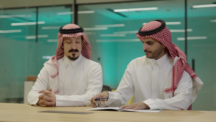 شركاء عمل يجتمعان في أحد الشركات، الشراكة على الأعمال و المشاريع التجارية، رجل عربي خليجي سعودي يتدي الثوب و الشماغ يقوم بتوقيع عقد عمل بسعادة، إتفاق عمل جديد ، صفقات عمل و تعاون بين الشركات