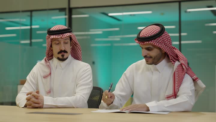 الشراكة على الأعمال و المشاريع التجارية، رجل عربي خليجي سعودي يتدي الثوب و الشماغ يقوم بالمصافحة وتوقيع عقد عمل بسعادة ، شركاء عمل يجتمعان في أحد الشركات  ، إتفاق عمل جديد ، صفقات عمل و تعاون بين الشركات