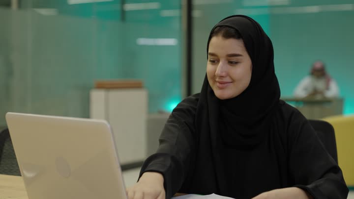 ادخال البيانات من خلال لوحة المفاتيح, تطور التكنولوجيا وإستخدام الأجهزة التقنية الحديثة,  امرأة عربية خليجية سعدية ترتدي العباءة السوداء تقوم بادارة الأعمال من خلال الحاسوب المحمول، كتابة وتدوين الملاحظات