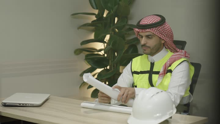 مهنة ووظيفة هندسية شبابية، إدارة المشاريع الهندسية، التصاميم المعمارية وتدقيق المخططات، تنمية وتطور العمل في المجال الهندسي, مهندس عربي خليجي سعودي يرتدي ستره الحماية يمسك بيدية مخطط الإعمار