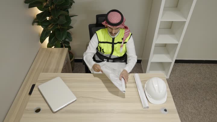 إدارة المشاريع الهندسية، التصاميم المعمارية وتدقيق المخططات، تنمية وتطور العمل في المجال الهندسي, مهندس عربي خليجي سعودي يرتدي ستره الحماية يمسك بيدية مخطط الإعمار