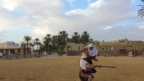 Two men dressed in traditional attire are sword fighting, an event in the Mamalik in the province of Tayma, the royal history of the ancient city of Tayma, the festival of ancient kingdoms, a theatrical performance, preserving the historical heritage.