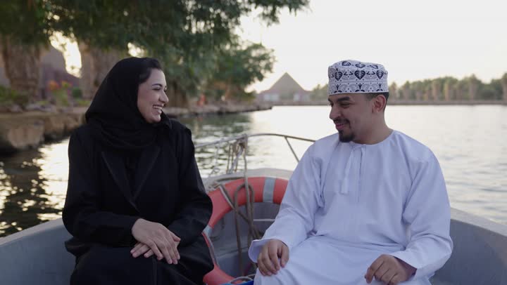 التقاط صور السيلفي التذكارية باستخدام الهاتف المحمول، توثيق اللحظات وبناء علاقات اجتماعية ناجحة، تقوية العلاقات الزوجية وروابط الحب والمودة، زوجان عربيان خليجيان عمانيان يرتديان الزي التقليدي يجلسان فى المركب ، تعابير السعادة و السرور