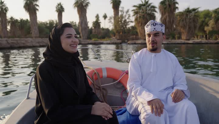 حوارات ونقاشات في الأجواء الطبيعية، قضاء وقت ممتع فى الخارج، ايماءات السعادة و السرور، رجل عربي خليجي عماني يرتدي الدشداشة والكمة يجلس فى الهواء الطلق على مركب برفقة زوجته