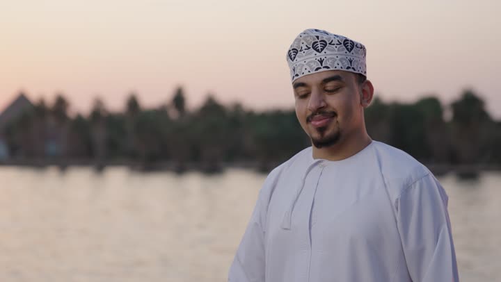 قضاء أوقات هادئة في الخارج، البهجة بقدوم شهر الخير، التحضير لاستقبال رمضان المبارك, تصوير مقرب لشاب عربي خليجي عماني يرتدي الدشداشة و الكمة يمسك فانوس معدني مزخرف, الاحتفال بالمناسبات الدينية الإسلامية, النظر للكاميرا بتعابير السعادة و السرور