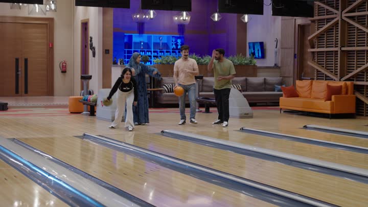 عائلة عربية خليجية سعودية تقضي أوقات مسلية أثناء ممارسة رياضة البولينغ ,الابن و الابنة يتنافسون بروح رياضية على الفوز ,الام و الاب يشجعون الأبناء بحماس وحب ,المنافسة في جو من الألفة و السعادة , نشاط ترفيهي عائلي في صالة البولينج